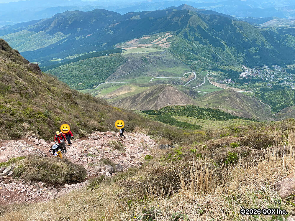 険しい山道と、背景には麓の街や近くの山が見えます