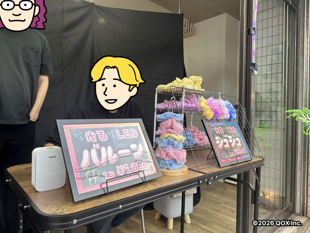 店のディスプレイを行った机に座るスタッフと、後ろに立って話すスタッフ
